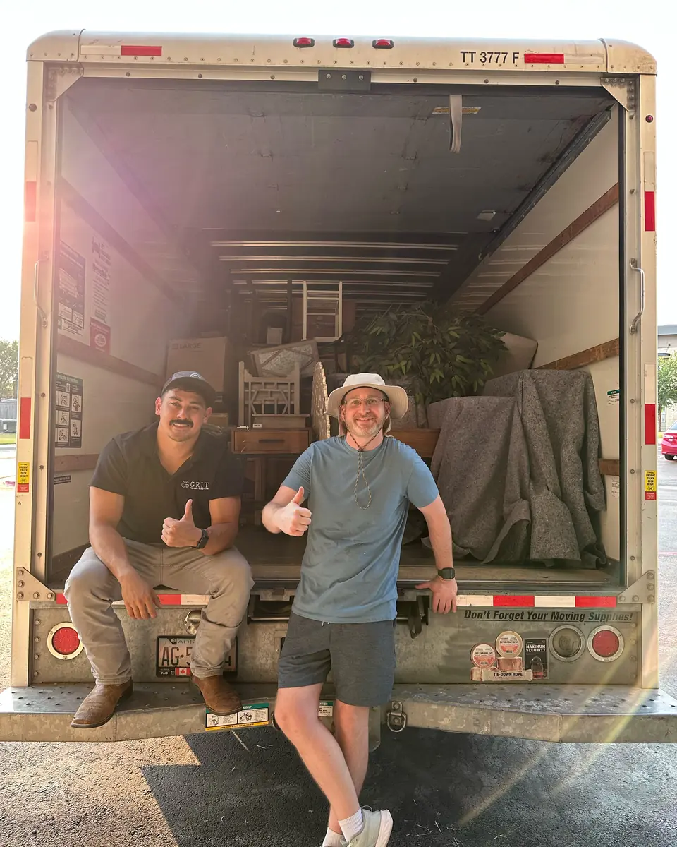 Two GRIT movers giving a thumbs up from the back of a packed moving truck